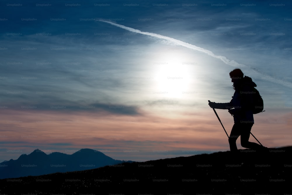 Silhouette eines Mädchens auf einem Berg während einer religiösen Wanderung in einem blauen und orangefarbenen Himmel.