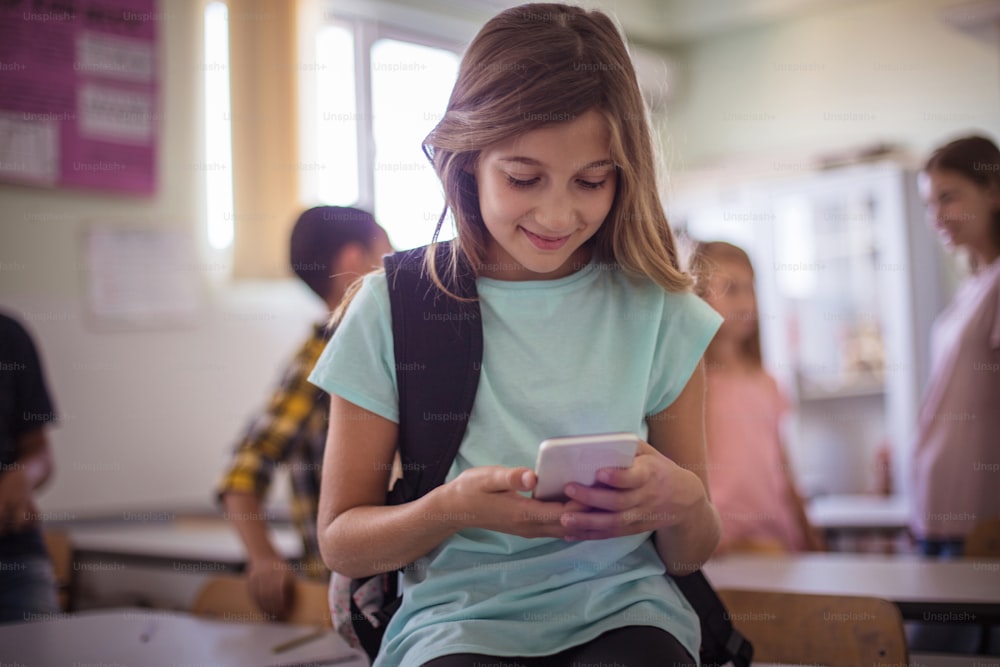 女子高生がスマートフォンでタイピング。 教室で電話を使う笑顔の女子高生。フォーカスは前景にあります。