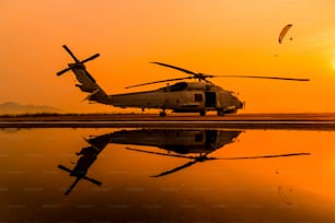 O estacionamento do helicóptero militar pousando na plataforma offshore, imagem de refecção no piso térreo e paraquedas voando no fundo do céu do pôr do sol