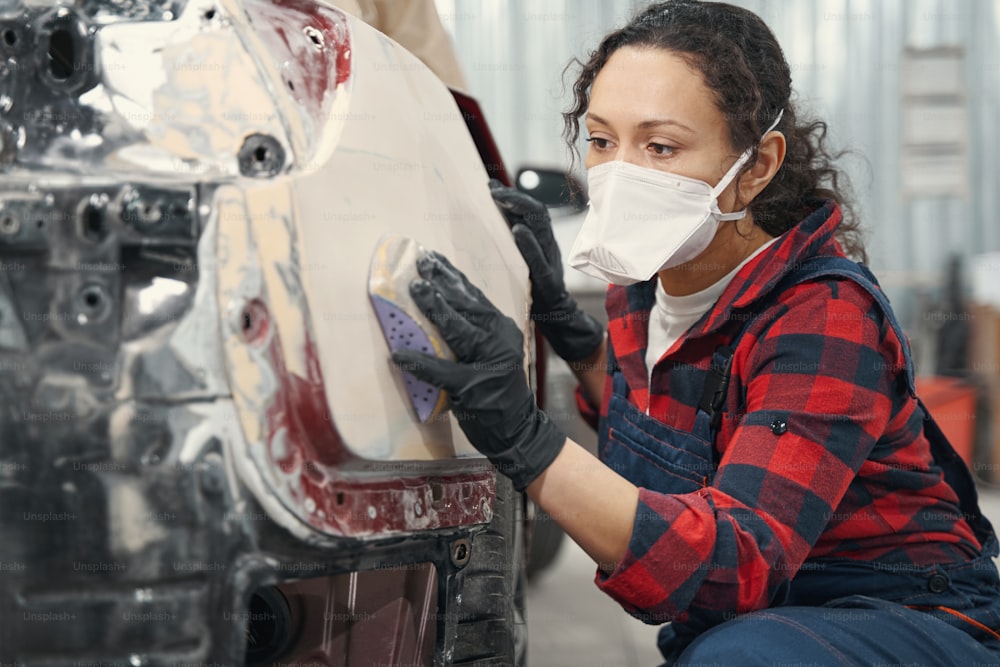 Attentive master wearing uniform while applying primer on car body