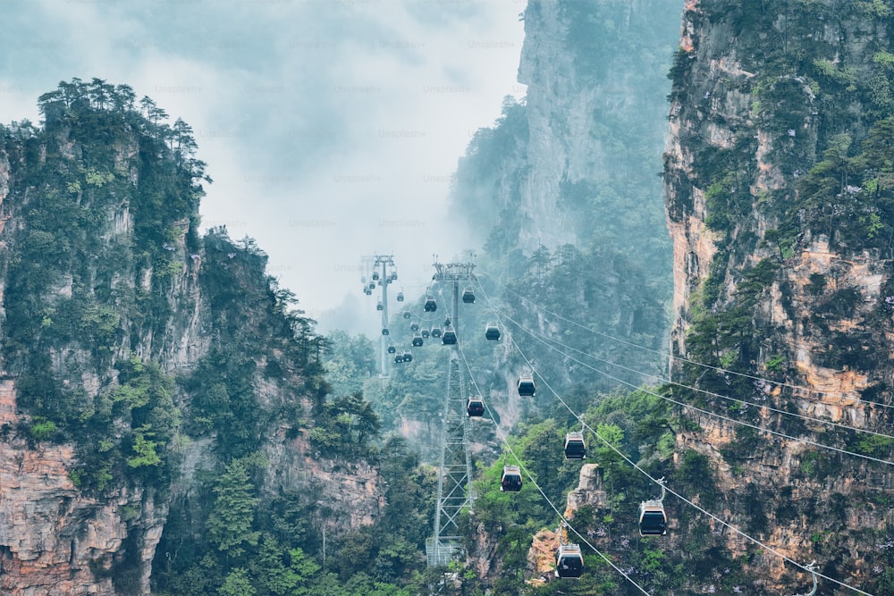 Famous tourist attraction of China - Zhangjiajie stone pillars cliff mountains in fog clouds with cable railway car lift at Wulingyuan, Hunan, China. With camera pan