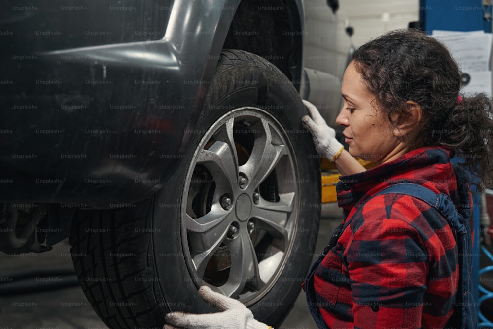 Técnico do veículo feminino em luvas de trabalho inspecionando a roda do automóvel na garagem do carro