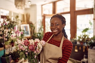 Retrato de florista afro-americana feliz com arranjo de flores frescas em sua loja olhando para a câmera.