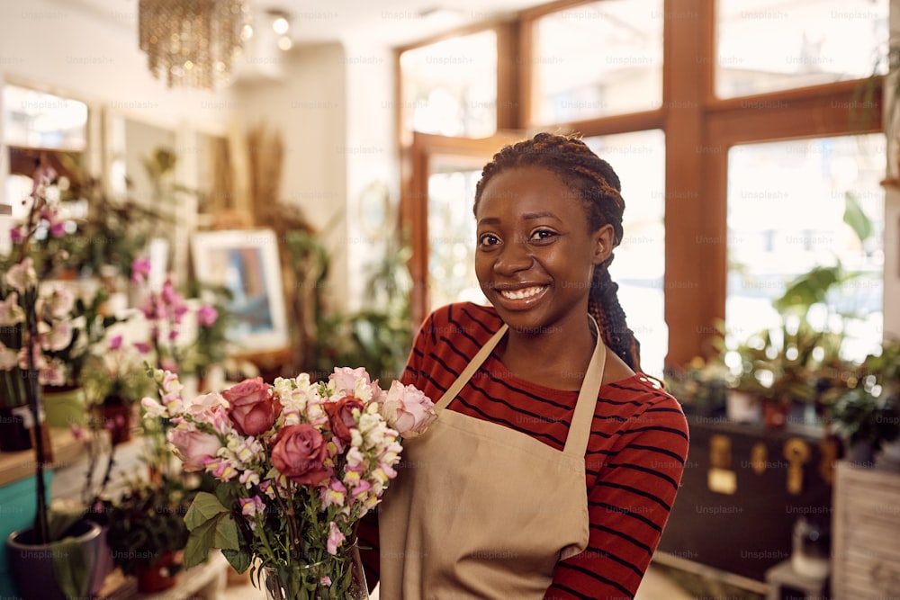 Portrait of happy African American florist with fresh flower arrangement at her shop looking at camera.
