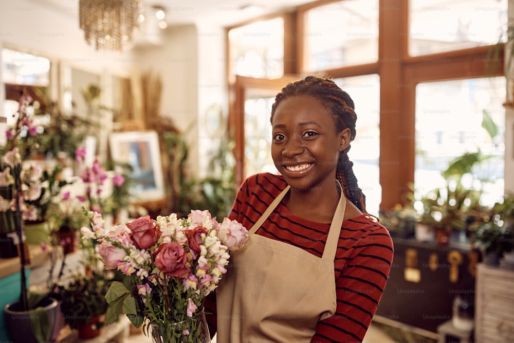 그녀의 가게에서 신선한 꽃꽂이를 하고 카메라를 바라보는 행복한 아프리카계 미국인 꽃집의 초상화.