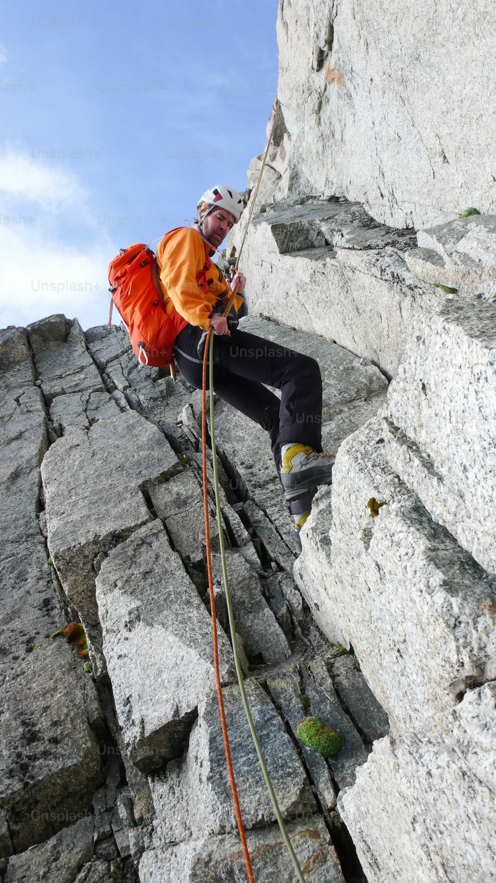 Um alpinista macho fazendo rapel em uma cordilheira rochosa íngreme nos Alpes franceses perto de Chamonix