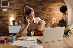 Working mother babysitting her small son while talking on the phone at home.