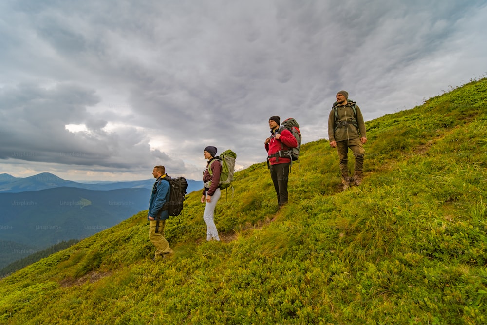 As quatro pessoas com mochilas de pé na montanha verde