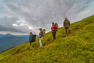 Les quatre personnes avec des sacs à dos debout sur la montagne verte