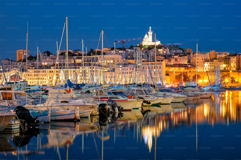 Porto Velho de Marselha (Vieux-Port de Marselha) com iates e Basílica de Notre-Dame de la Garde à noite. Marselha, França