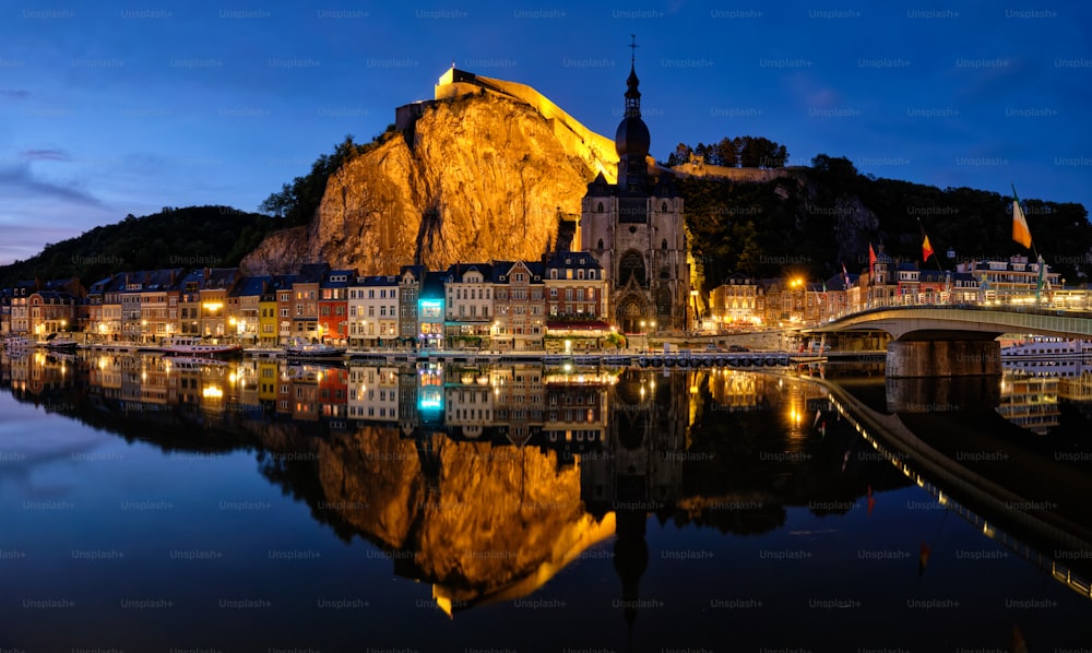 Nachtansicht der Stadt Dinant, der Stiftskirche Notre Dame de Dinant über die Maas und die Brücke Pont Charles de Gaulle und die Zitadelle von Dinant, die am Abend beleuchtet werden. Dinant, Belgien