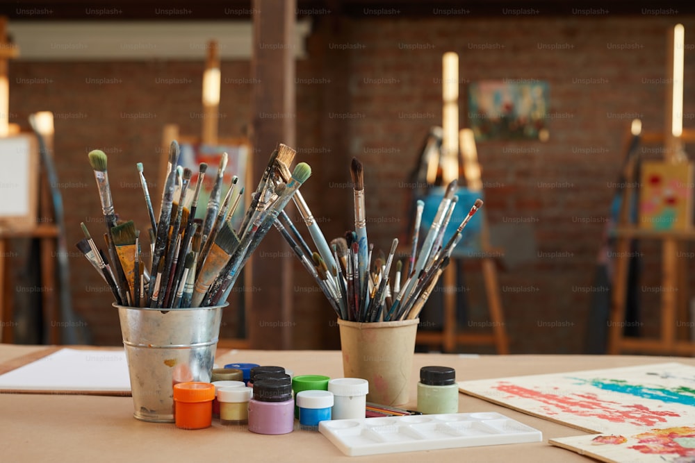 Imagem de diferentes tipos de pincéis com tintas coloridas e imagens estão na mesa na oficina