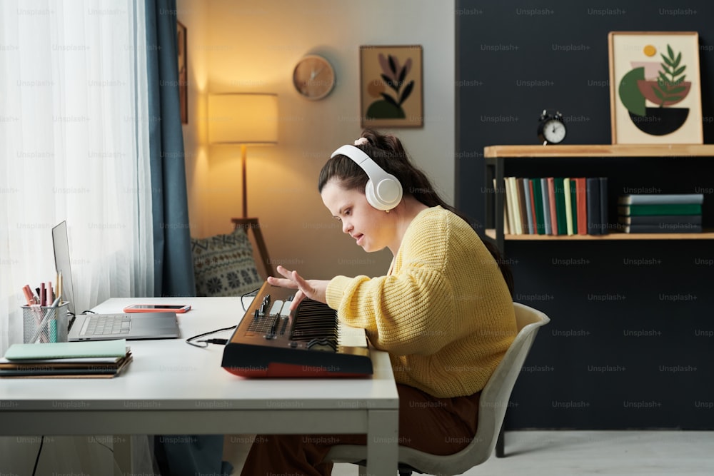 Vista lateral de mulher caucasiana jovem com síndrome de down usando fones de ouvido aprendendo a tocar teclado eletrônico