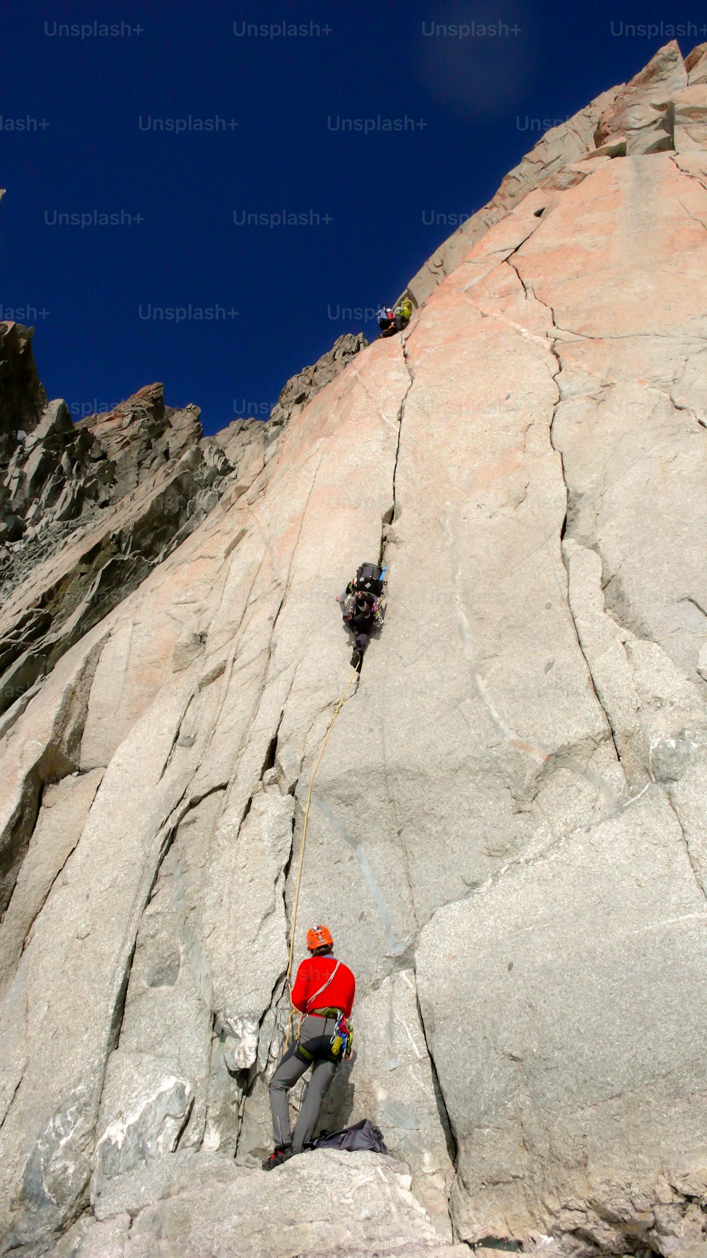 青空の下、シャモニー近郊のフレンチアルプスの花崗岩の壁の険しいルートを走る2人のロッククライマー