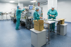 Pharmaceutical technicians work in sterile working conditions at pharmaceutical factory. Scientists wearing protective clothing