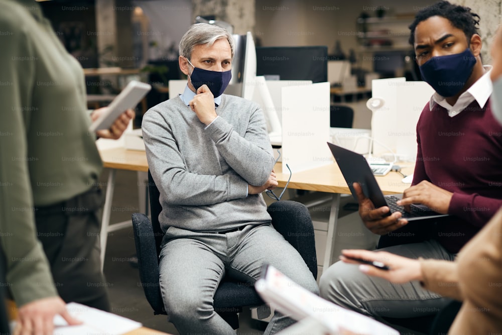 Gruppo di imprenditori che indossano maschere per il viso durante la riunione di lavoro presso l'ufficio aziendale. L'attenzione è rivolta all'uomo d'affari maturo.