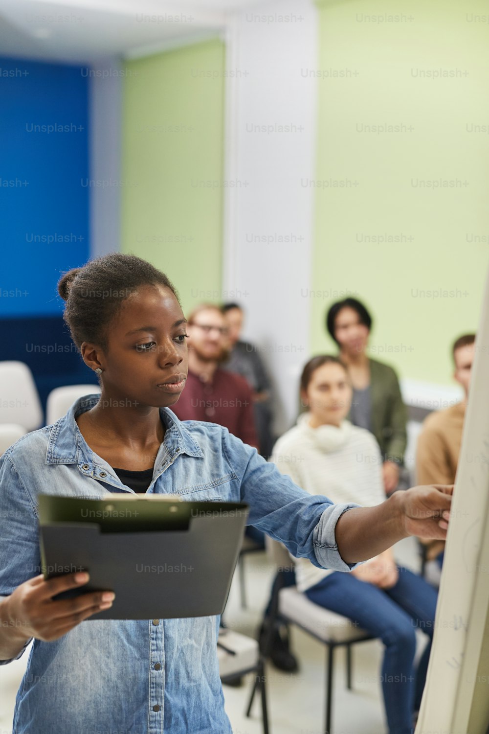 Young African teacher standing near the whiteboard and explaining the new material to the students