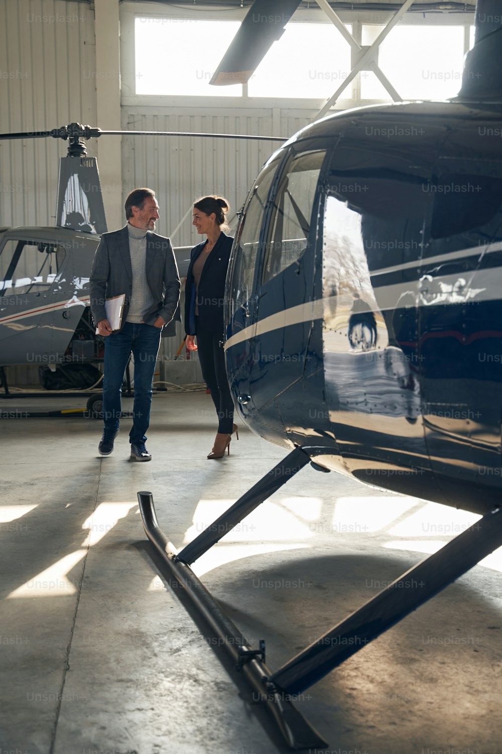 Smiling mature male and joyous stylish young female having conversation in aircraft hangar