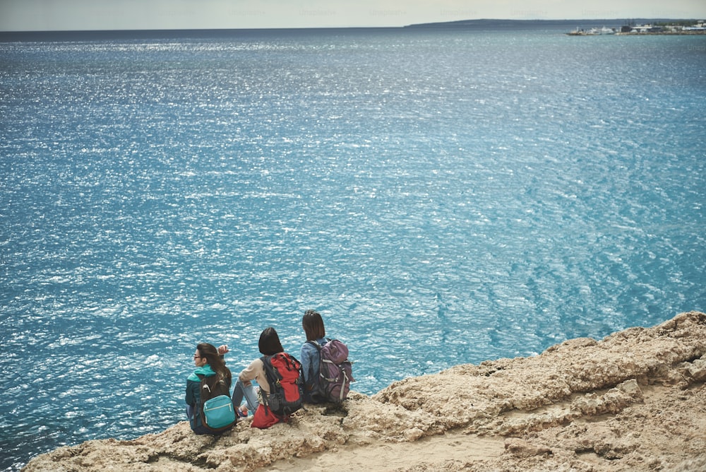 素晴らしい風景。穏やかな女性旅行者が水辺の崖でくつろいでいます。果てしなく続く海を感嘆の眼差しで見つめている
