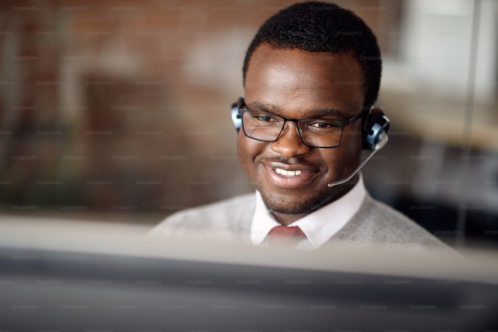Happy African American businessman talking via headset while working on a computer in the office.