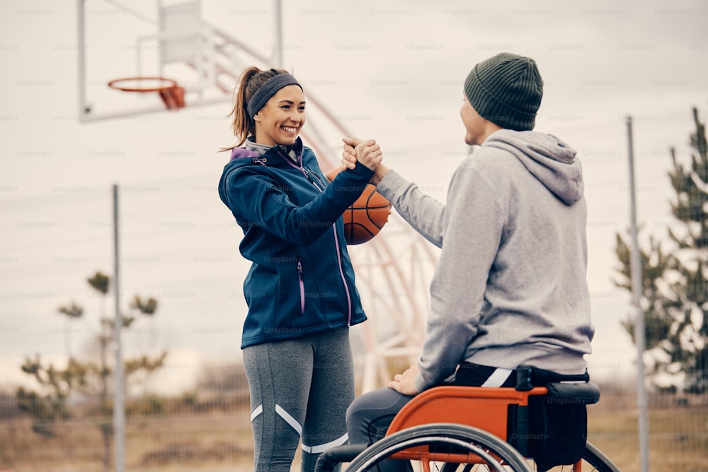 Atleta masculino con discapacidad y su amiga felicitándose después de jugar baloncesto en una cancha al aire libre. El foco está en la mujer.