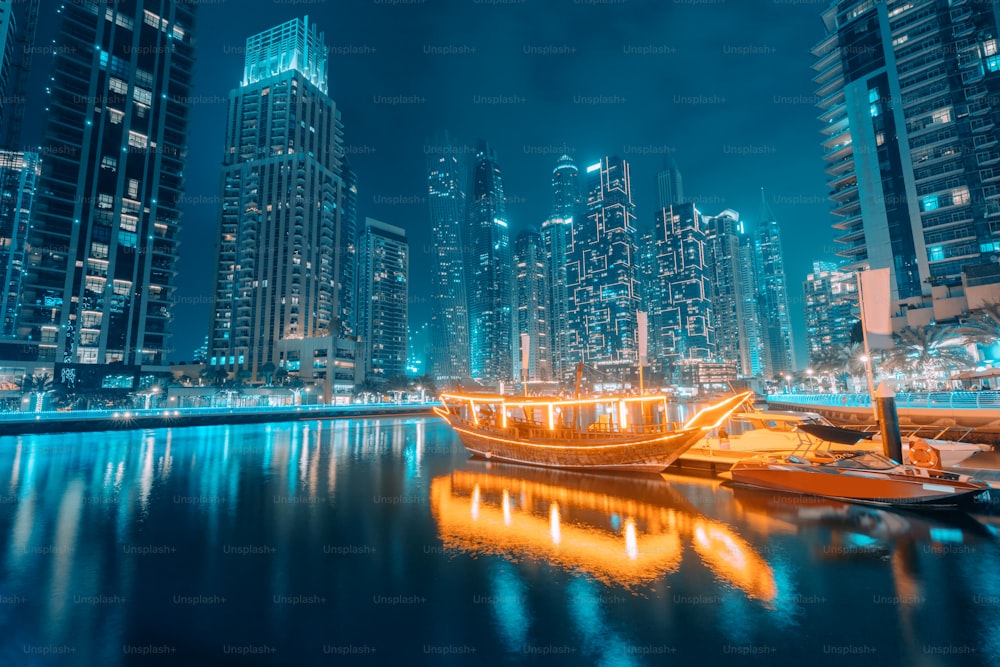 Iluminado por inúmeras luzes, o ferry ship estilizado como um tradicional barco árabe Abra Dhow navega pelas águas da Marina de Dubai