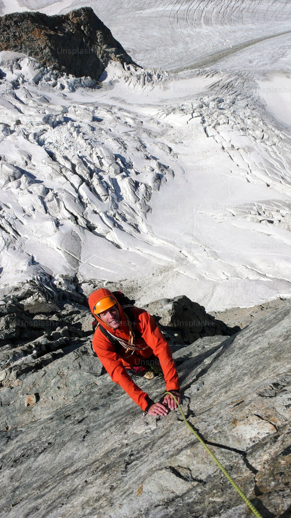männlicher Bergsteiger auf einer exponierten Kletterroute hoch über einem Gletscher in den Schweizer Alpen bei St. Moritz