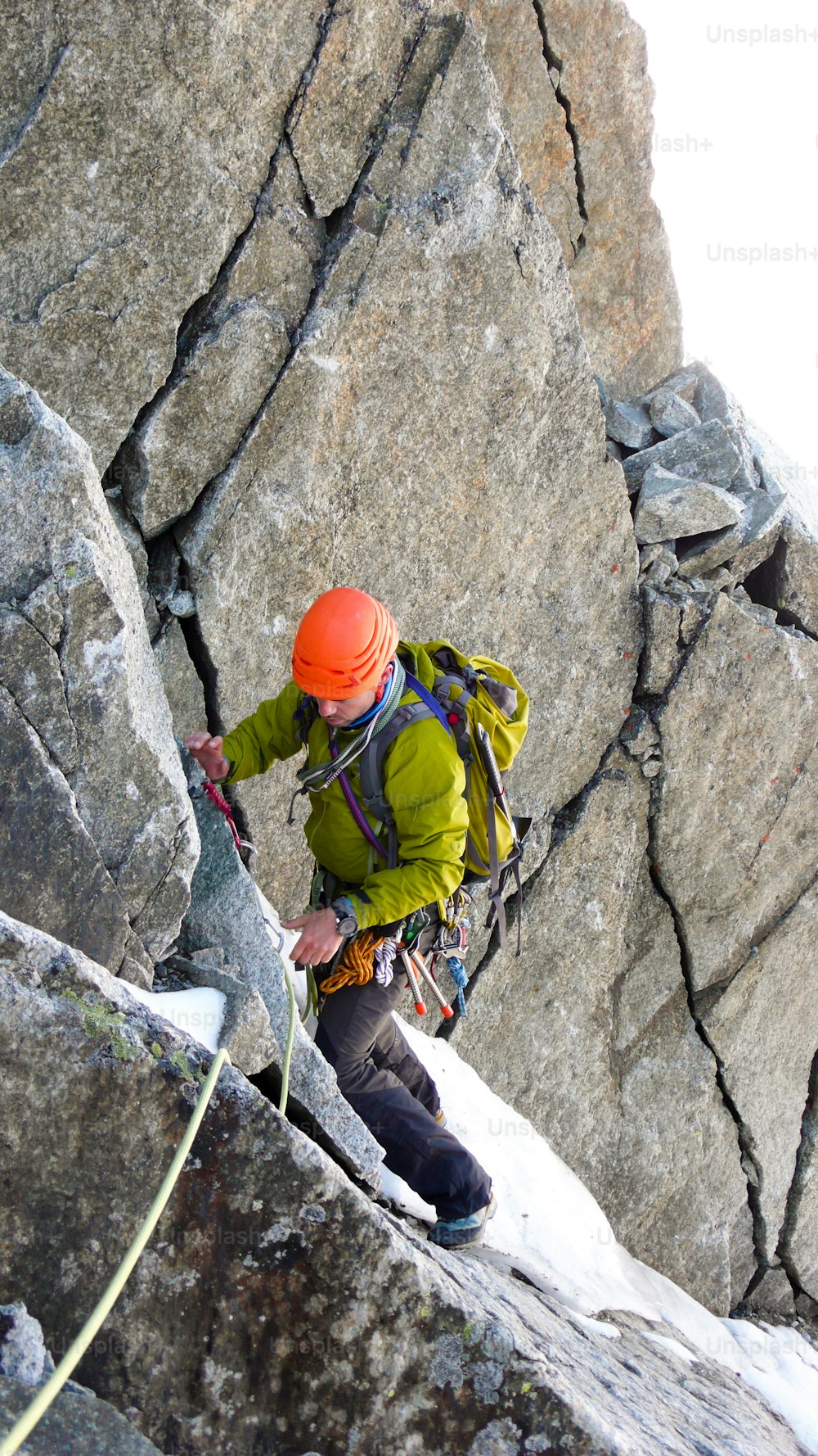 A male mountain climber traverses a tricky rock chimney on his way to a high alpine summit