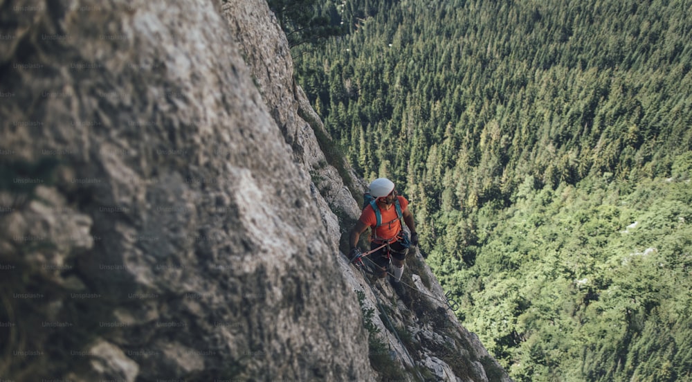 Climber on via ferrata trail, crossing a steep mountain edge.