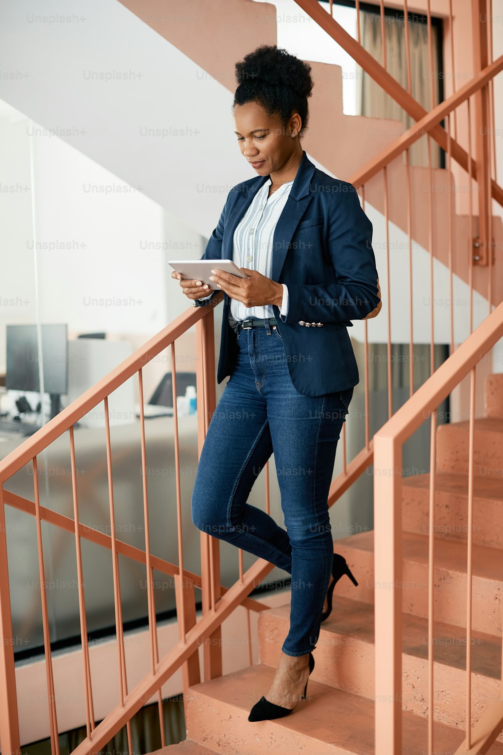 African American businesswoman reading an e-mail on touchpad on staircase in a hallway.