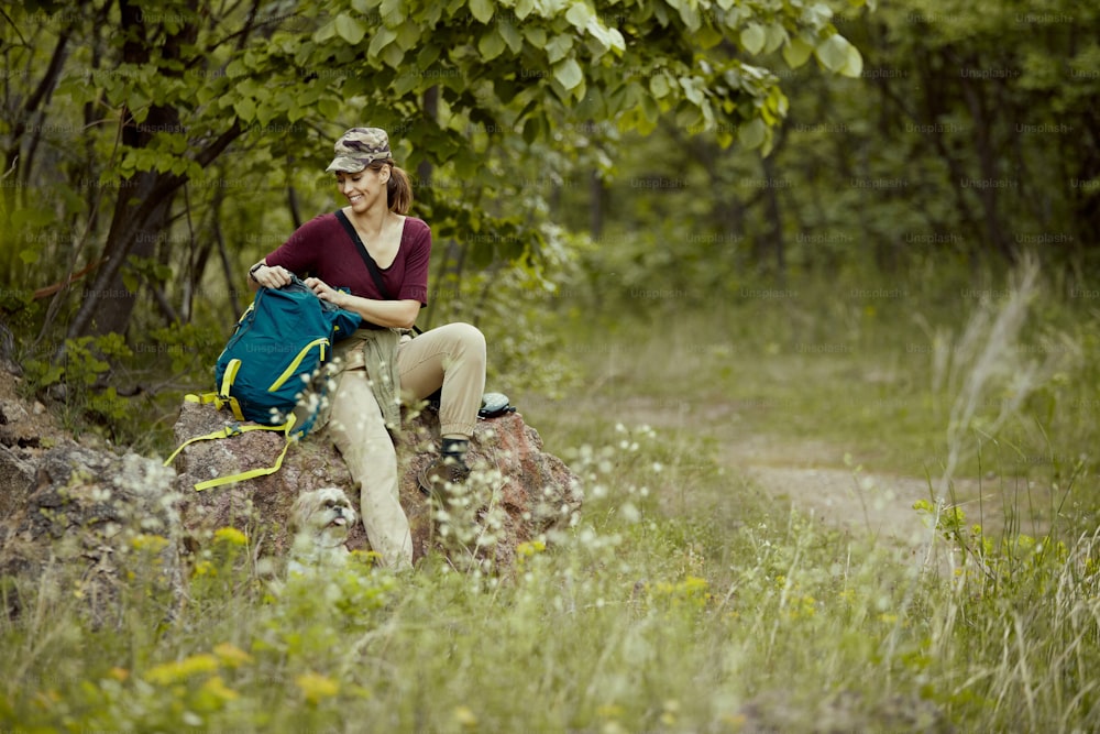 Felice backpacker femmina con cane che si rilassa dopo un'escursione nei boschi. Copia spazio.