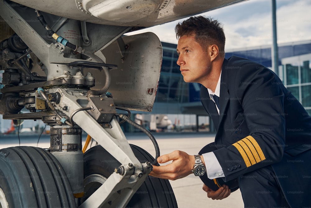 Side view of a focused male pilot in uniform performing a visual inspection of undercarriage