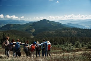 Vista traseira de jovens turistas ativos que se ligam uns aos outros enquanto desfrutam de uma bela paisagem da colina da montanha