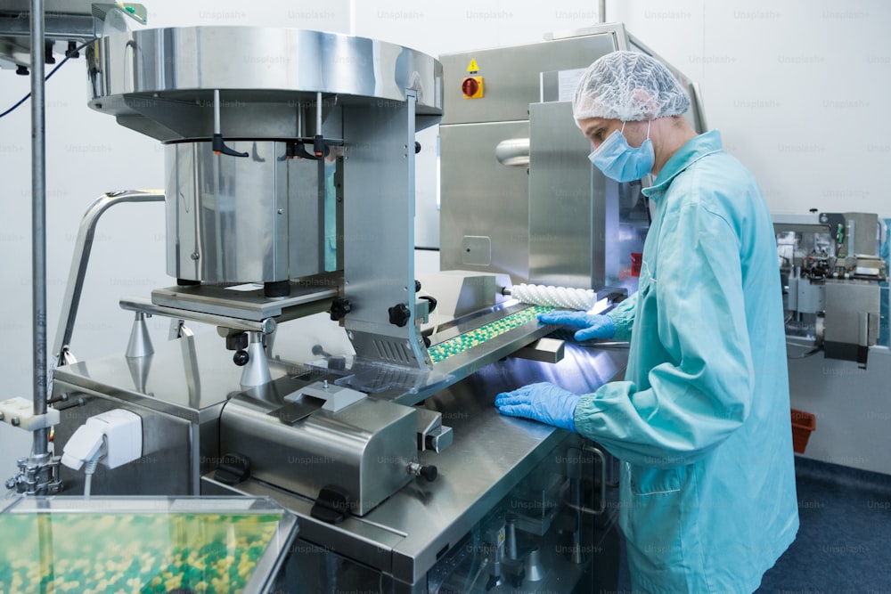 Pharmaceutical technician in sterile environment working on production of pills at pharmacy factory