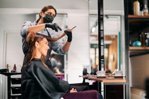 Friseur, der Frauen in einem Salon die Haare schneidet und aufgrund der Coronavirus-Pandemie eine Gesichtsmaske trägt.