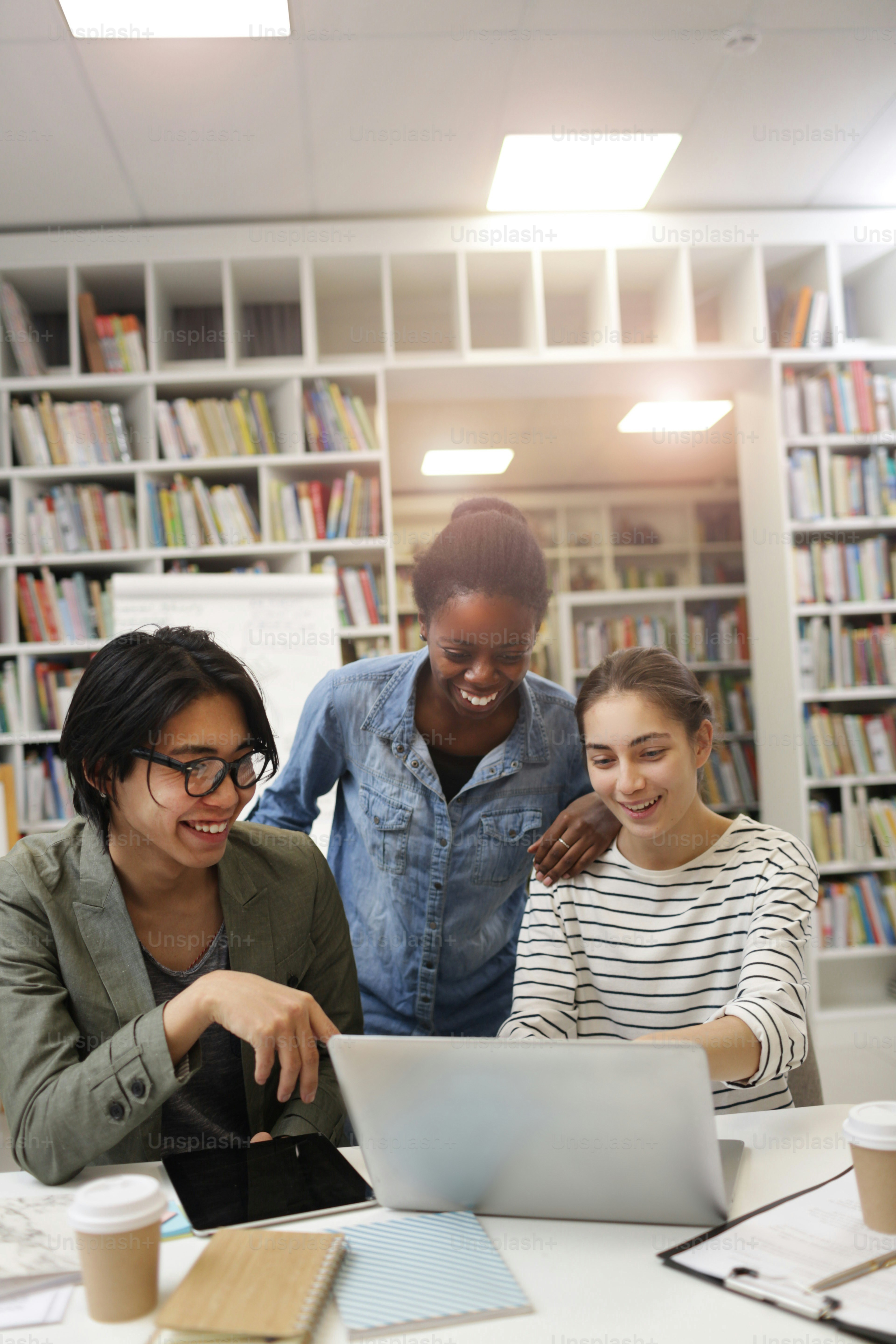 Group of young people laughing while watching online presentation on laptop at the table in the library