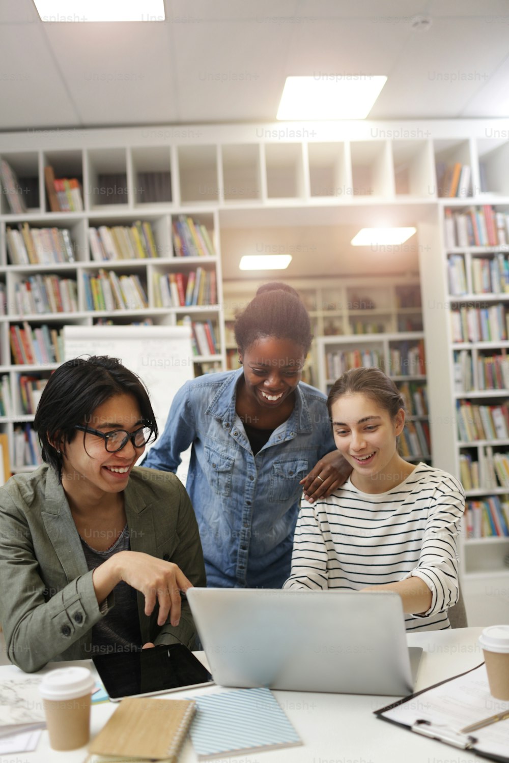 Grupo de jóvenes que se ríen mientras ven la presentación en línea en una computadora portátil en la mesa de la biblioteca