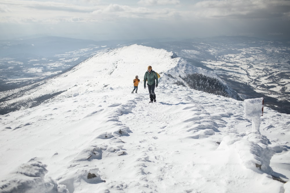 Two hikers ascending over snowy mountain ridge.