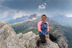 Une jolie alpiniste brune assise sur un sommet de montagne et souriante