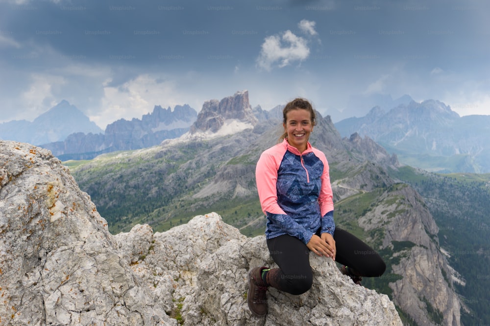 Un attraente alpinista bruno seduto su una cima di montagna e sorridente