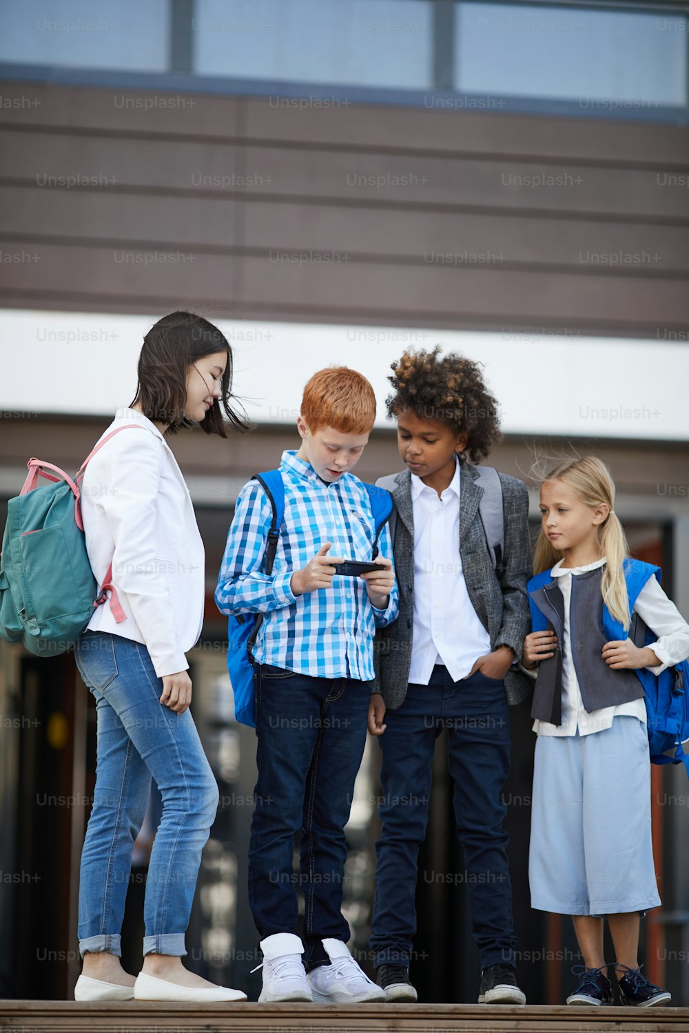屋外で学校の入り口付近に立ちながら携帯電話で一緒に遊んでいる小学生のグループ