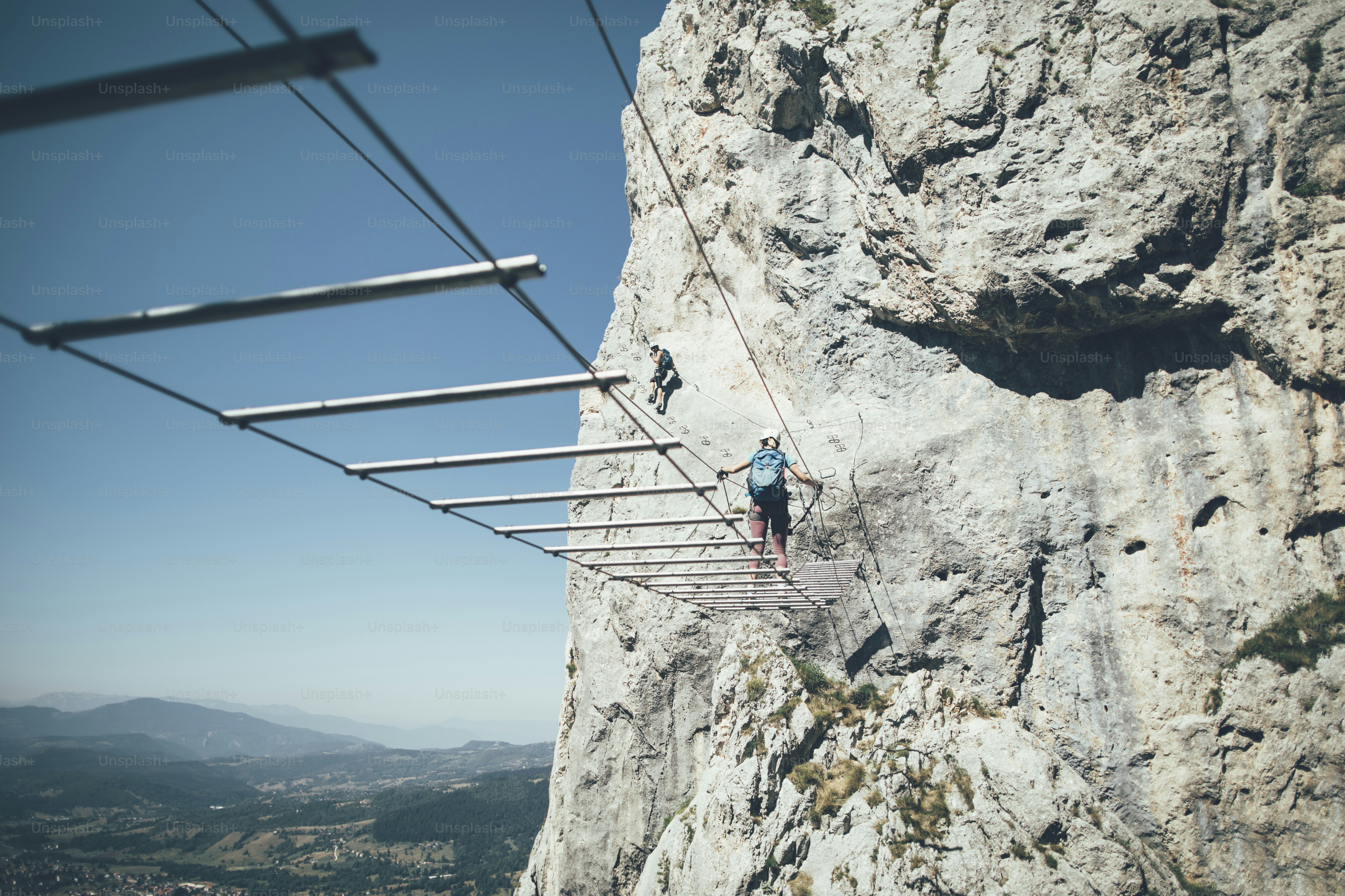 Two women climbers moving up and crossing wire bridge on via ferrata route.