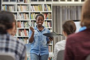 Lächelnde junge Afrikanerin präsentiert ihren Bericht dem jungen Publikum bei einer Präsentation in der Bibliothek