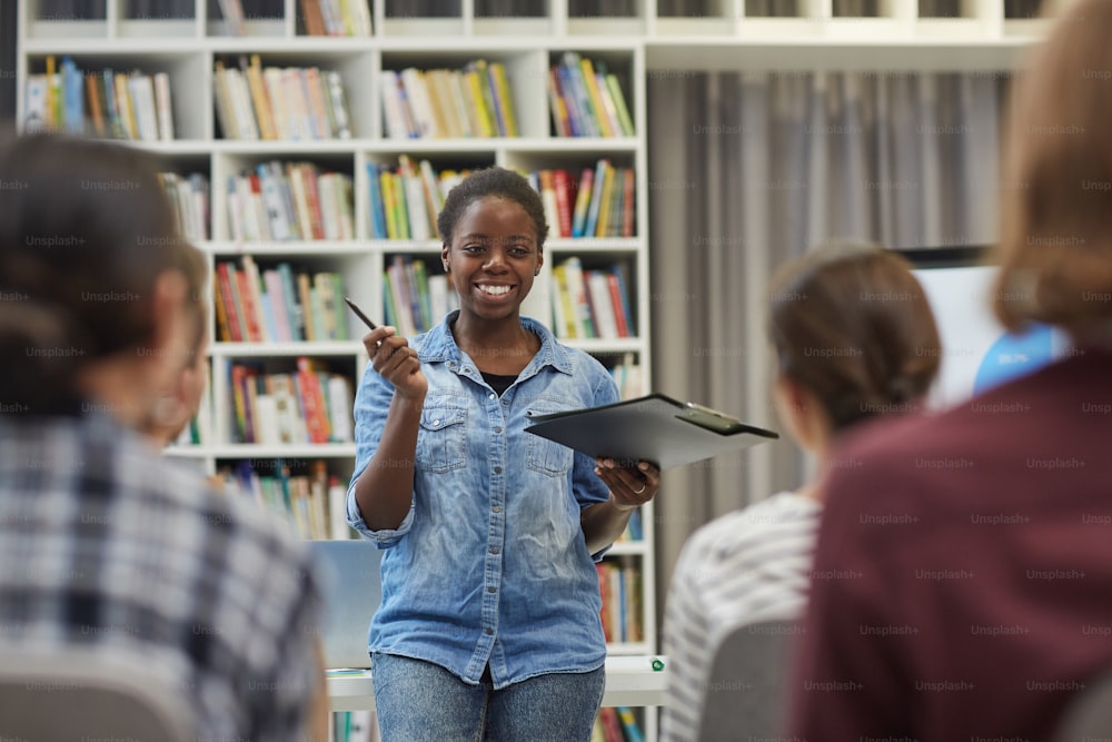 웃고 있는 젊은 아프리카 여성이 도서관에서 발표할 때 젊은 청중에게 보고서를 발표하고 있다