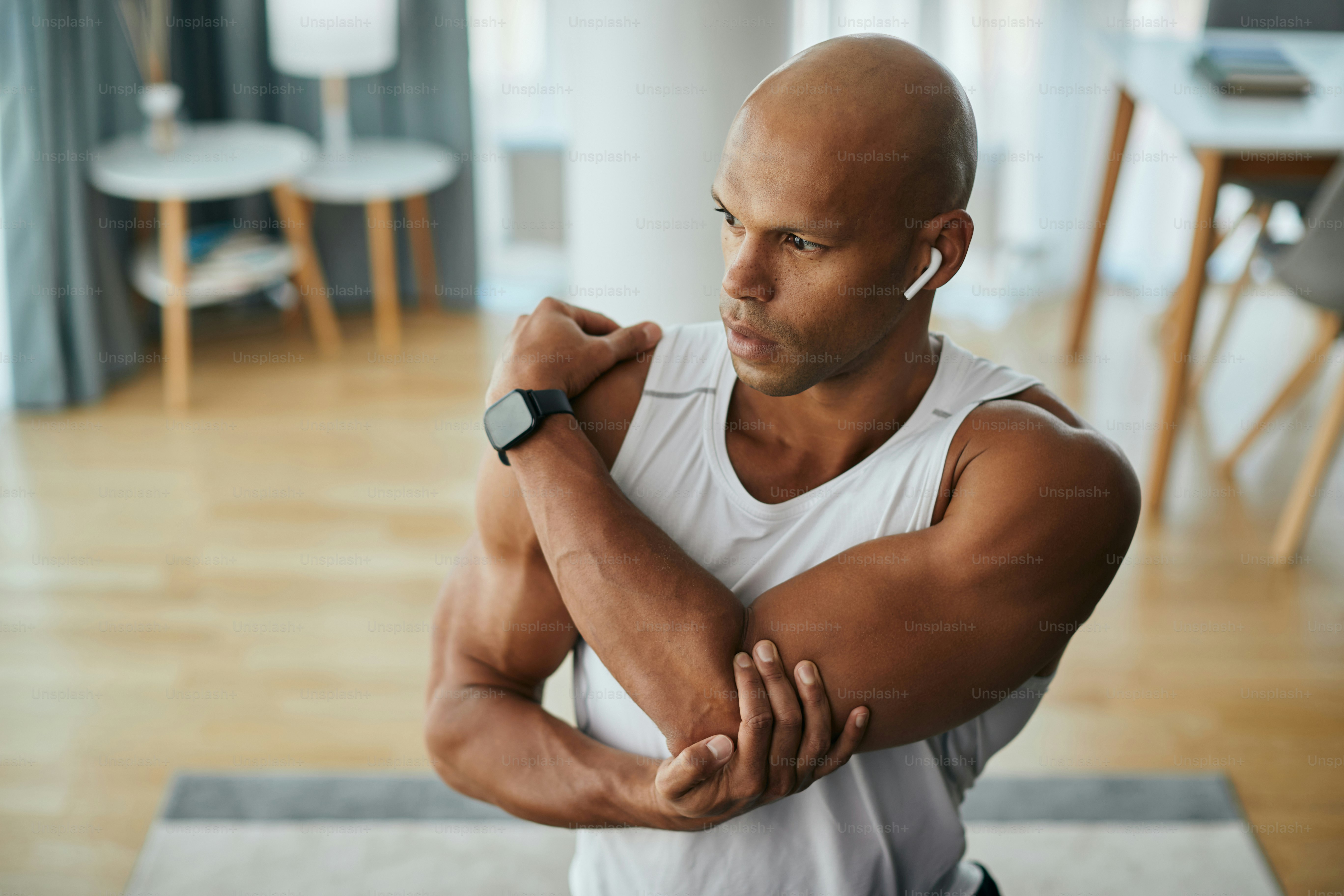 African American athlete warming up for home workout and stretching his arm.