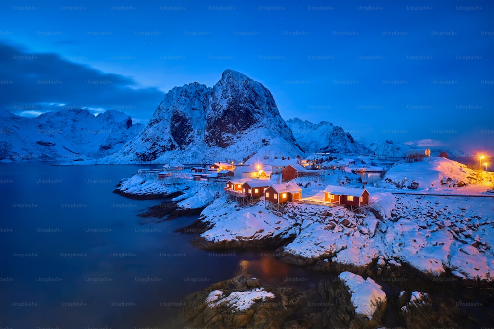 Famous tourist attraction Hamnoy fishing village on Lofoten Islands, Norway with red rorbu houses in winter snow illuminated in the evening