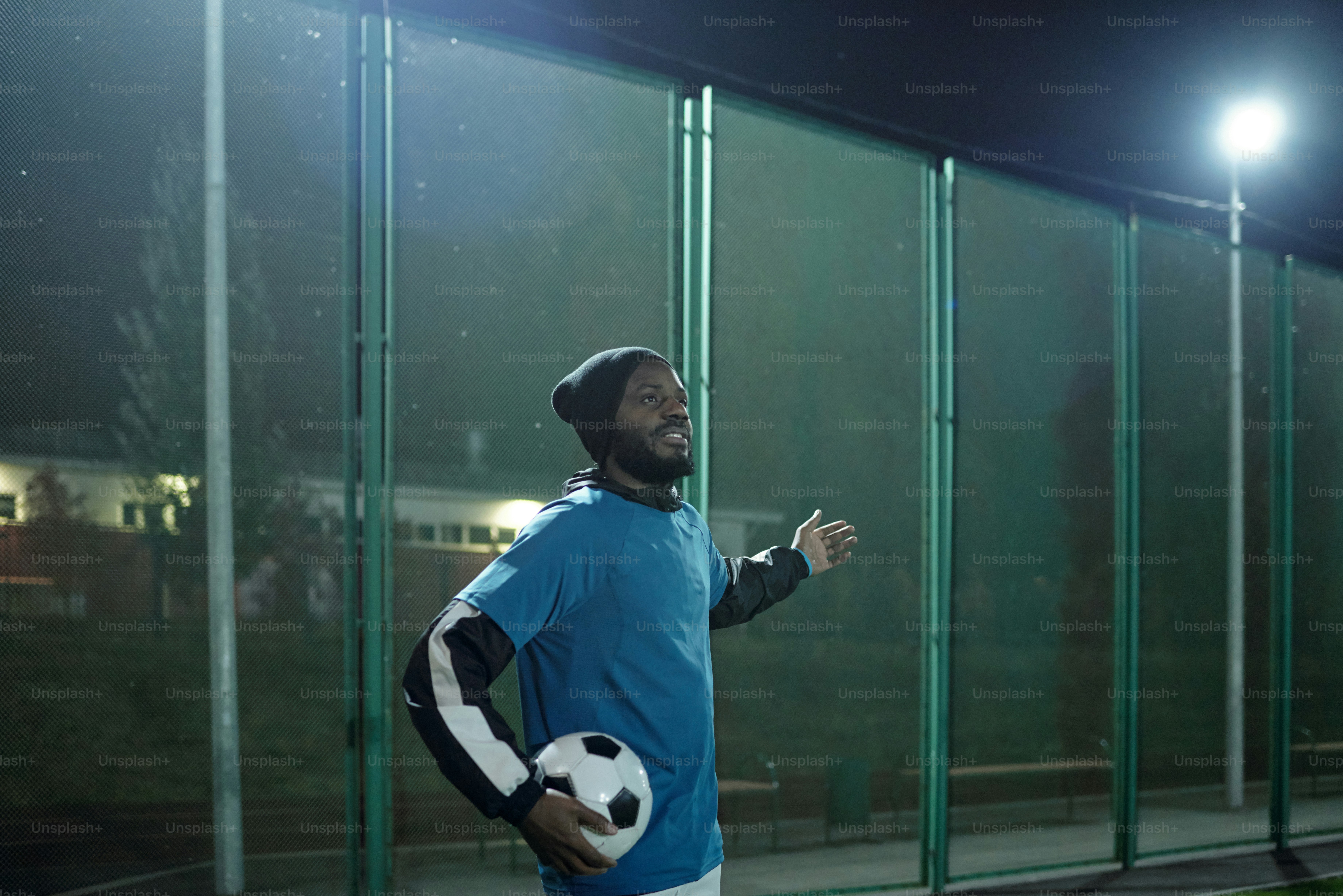 Young successful football trainer in professional sports uniform holding soccer ball while standing in front of large stadium