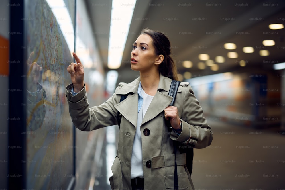 Mulher jovem olhando para o mapa do transporte público enquanto espera pelo trem no metrô.