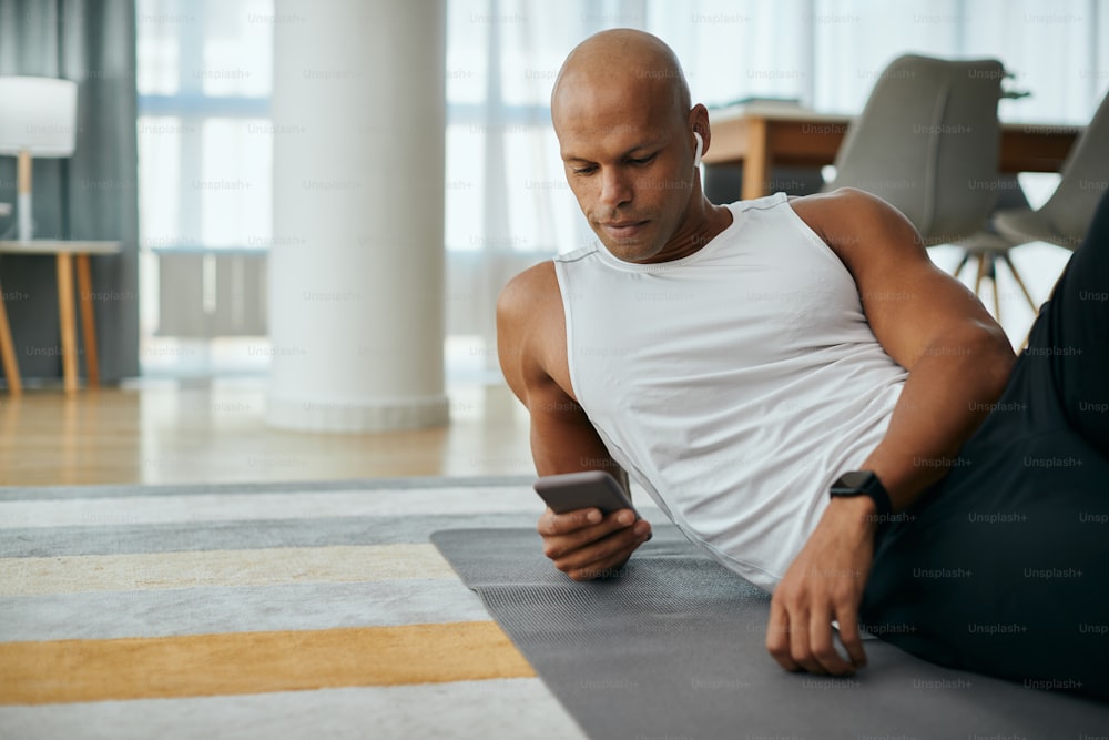 Smiling African American athlete texting on cell phone after exercising in the living room.
