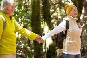 Happy caucasian senior couple with backpack walking in the forest enjoying healthy lifestyle and retirement